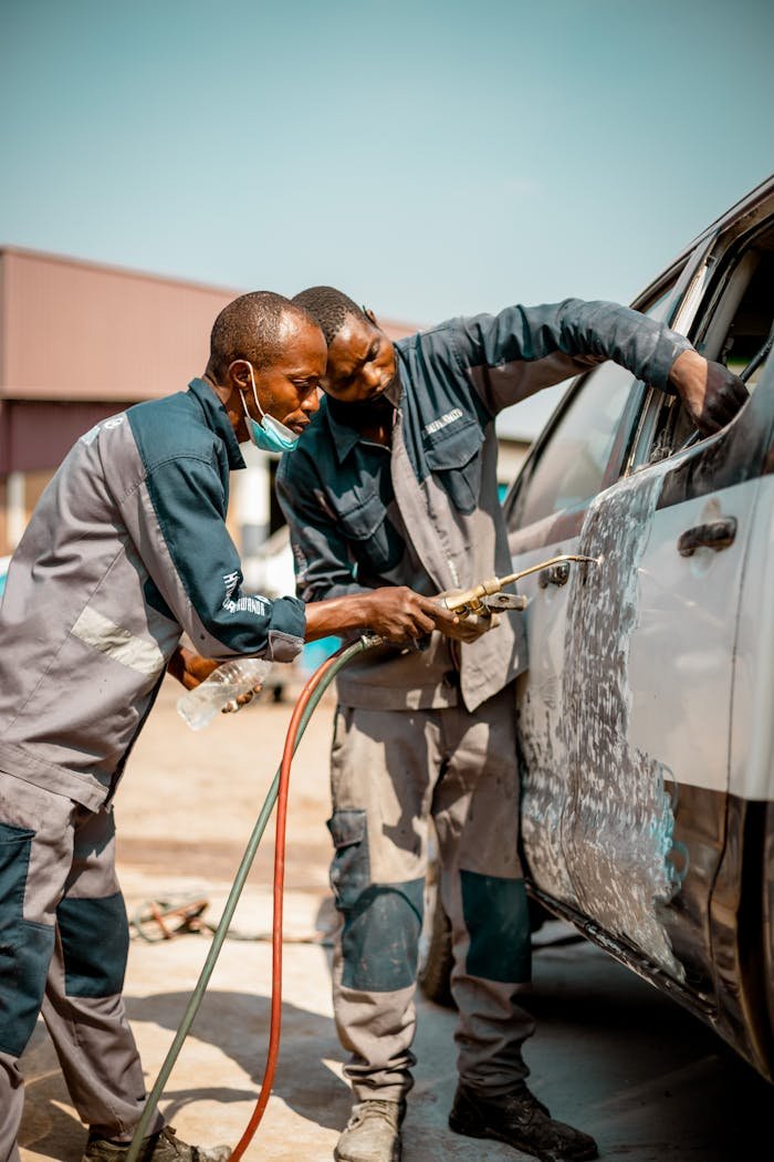 Two professionals cleaning a vehicle at an outdoor car wash station on a sunny day.